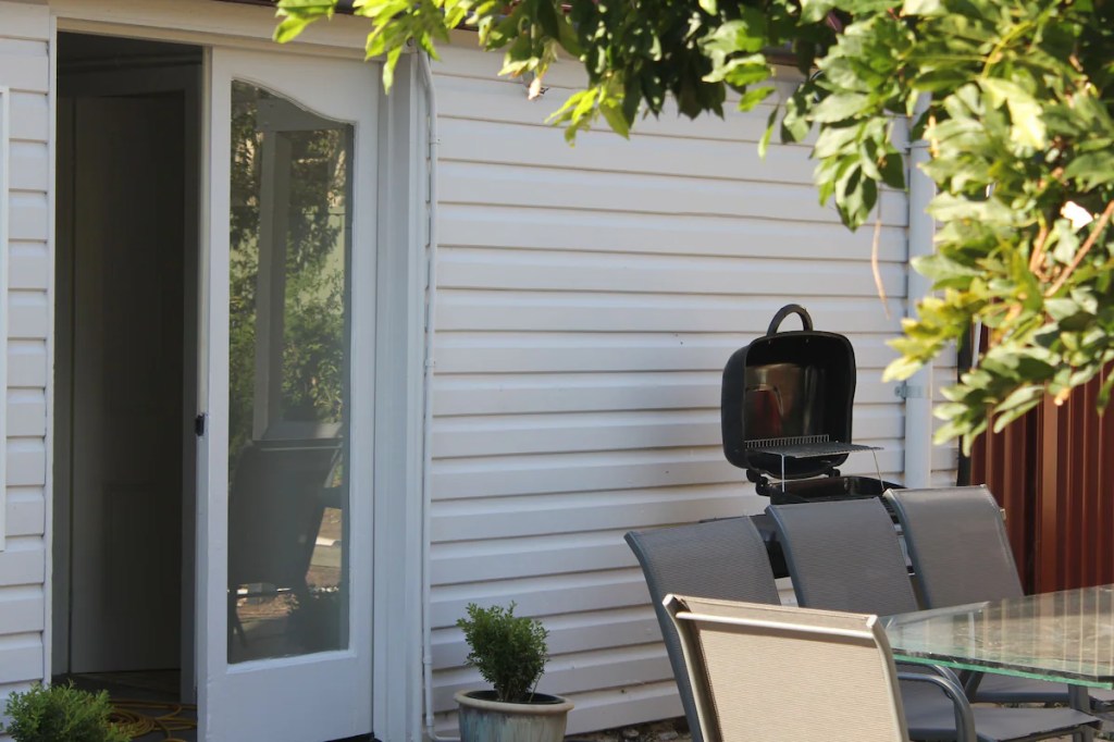 Image of outdoor dining table, BBQ and open read door into Merala accomodation.