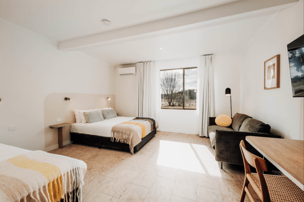 The Cudgee at Mudgee bedroom with double bed, lounge and desk. In the background a window shows the view to the river. 