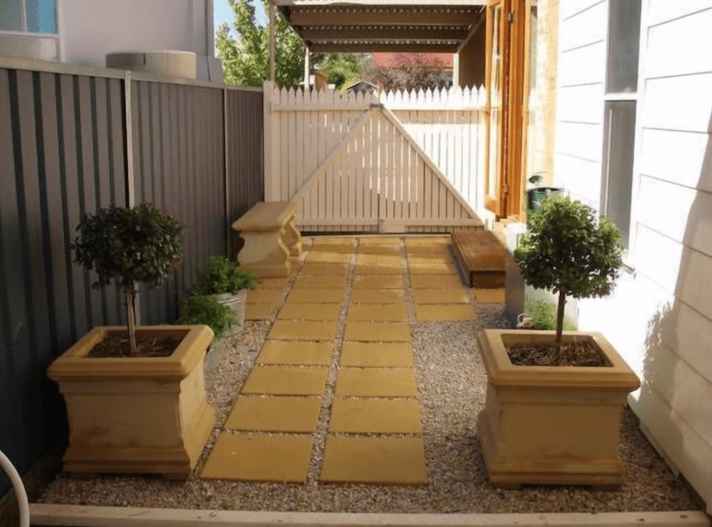 Side yard of Douro Cottage, Central Mudgee. Cement tiles and pebbles lead to a large white, secure gate in the background. 